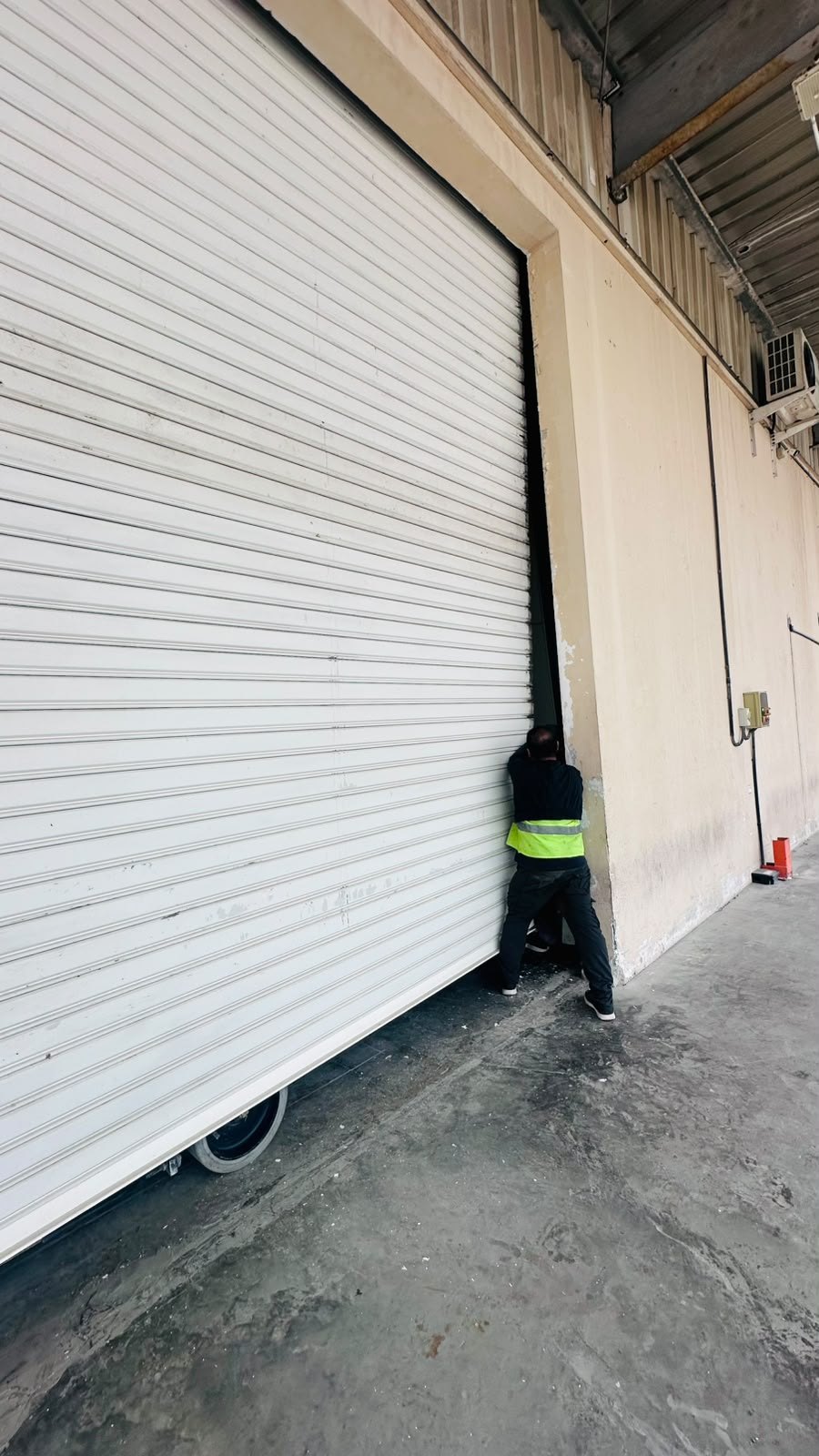 Technician repairing a large white rolling shutter at a warehouse in Dubai Investments Park 1