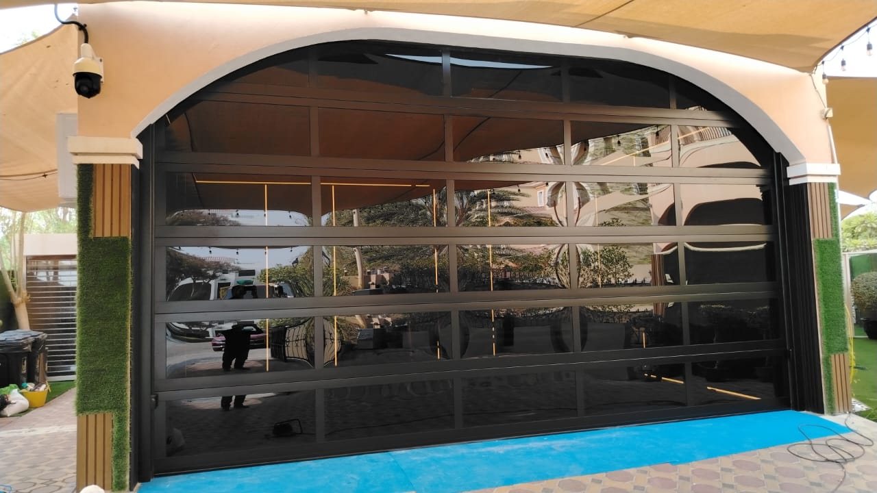 Panoramic glass garage door with dark aluminium frame in an arched opening of a Dubai villa