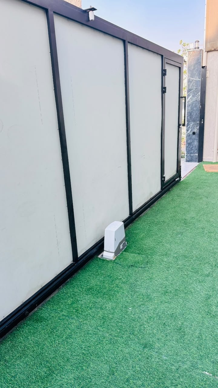 Sliding gate motor installed at the foot of a black steel sliding gate with a pedestrian door, Al Yasmeen, Ajman